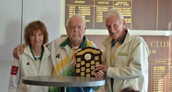 Man holds trophy up at bowl's club, supported by a man and woman on each side
