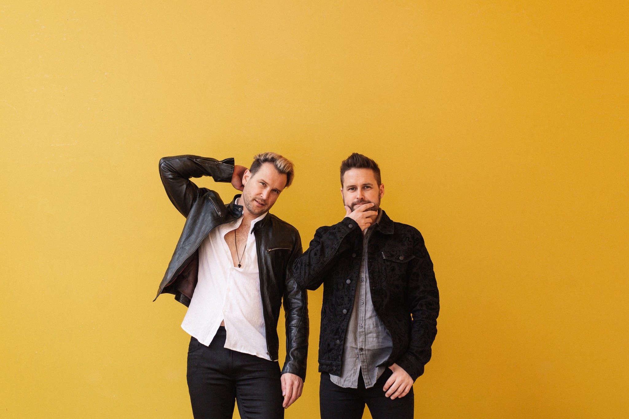 Two male music artists looking into the camera against an orange backdrop