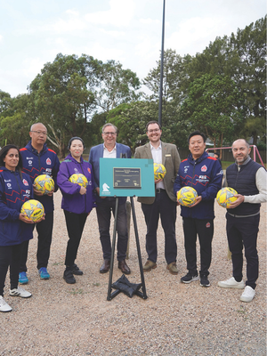 People gathered in a group holding soccer balls behind a Whitehorse branded lecturn. 