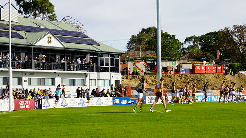 a football match in progress with members of the public watching from the pavilion