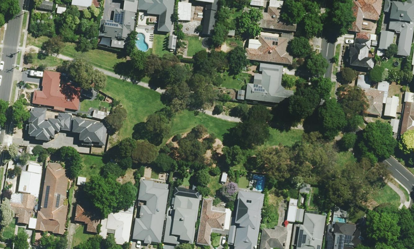 Aerial image of housing surrounding a strip of grassed area with established sparse tree canopy