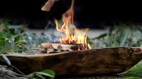wooden vessel sitting in a pile of eucalyptus with a small fire in the bowl of the vessel
