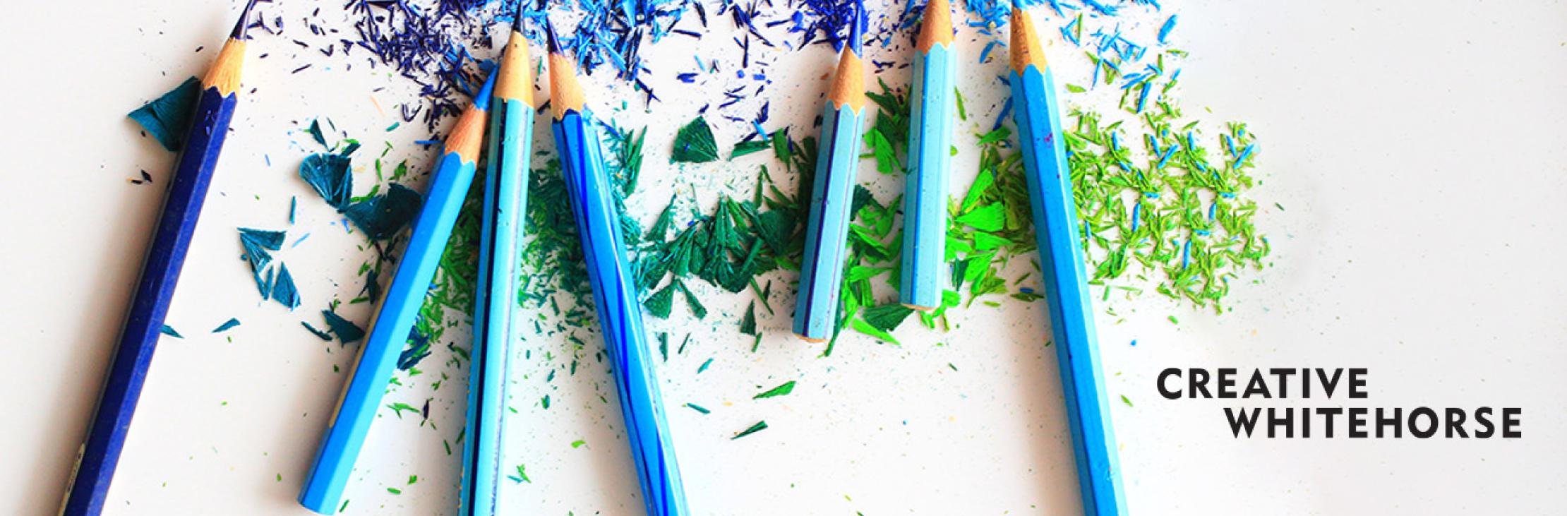 Sharpened shades of blue and green pencils with coloured shavings in background