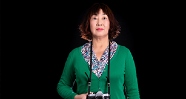 Asian women on black backdrop with green cardigan holding a camera