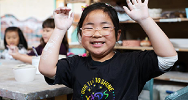 Young child smiling at the camera with clay on her outstretched hands 