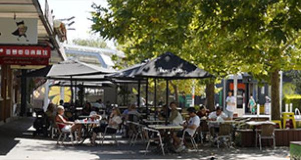 looking down Britannia Mall with shops on the left and people sitting on tables in the mall