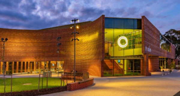 Landscape image of The Round at twilight. The low lighting highlighting the red bricks and The Round logo is lit yellow