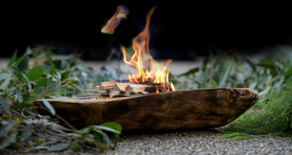wooden vessel sitting in a pile of eucalyptus with a small fire in the bowl of the vessel