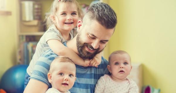 Dad with two children on lap with older child hugging him from behind
