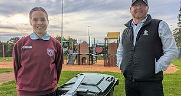 Man and girl smiling standing next to a bin at a park