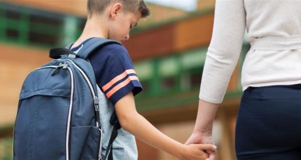 Young child who is hesitant about going to school, holding parents hand