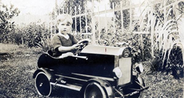 Black and white photo of small child in a fancy old fashioned toy car