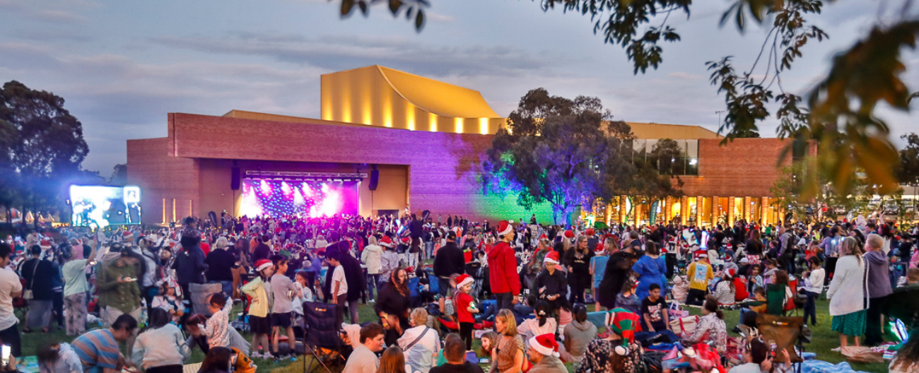 large crowd of people in Santa hats watching a colourful stage of performers