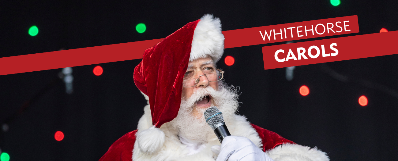 Santa singing into microphone with red  Whitehorse carols banner 