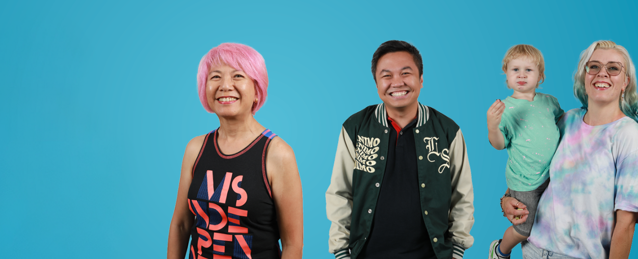 3 people and a baby standing in front of a blue background smiling. 