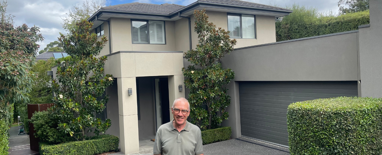 Geoff stands in front of grey house