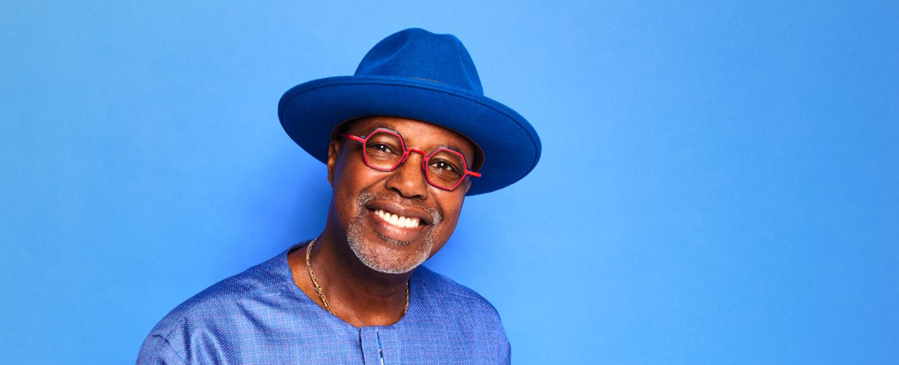 Man with red -rimmed glasses and blue hat smiles at camera