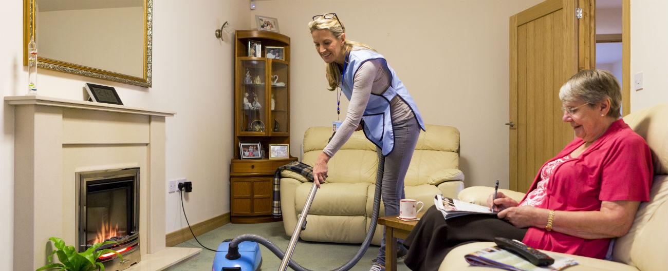 Support worker vacuuming with older woman