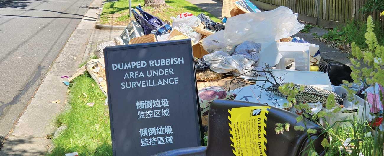Pile of dumped rubbish with a 'dumped rubbish under surveillance' sign 