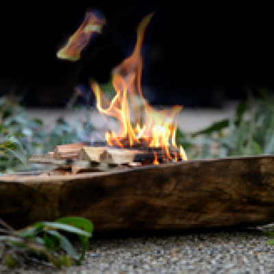 wooden vessel sitting in a pile of eucalyptus with a small fire in the bowl of the vessel